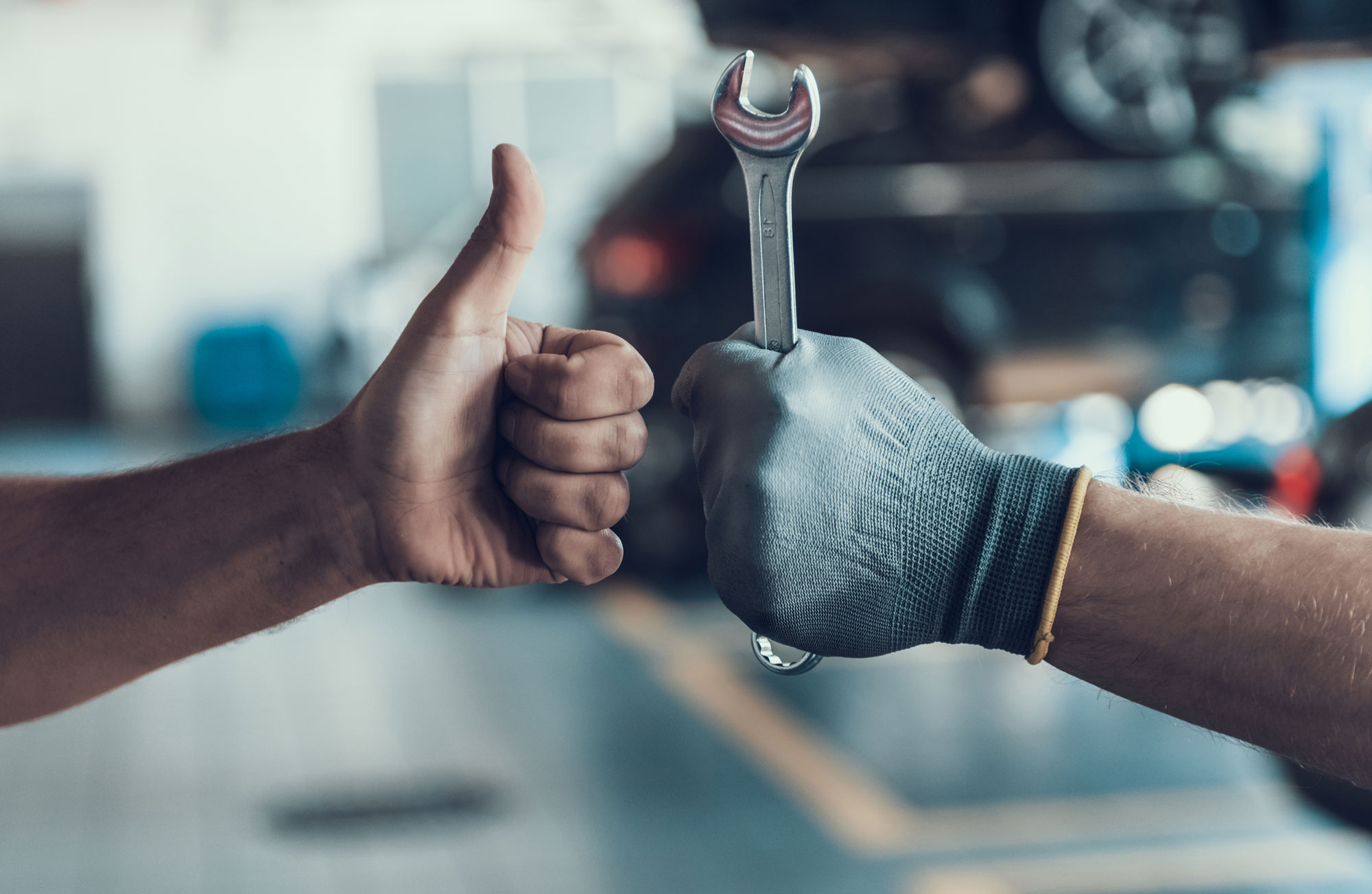 Two hands, one giving a thumbs up, the other holding a wrench, symbolizing approval and expertise
